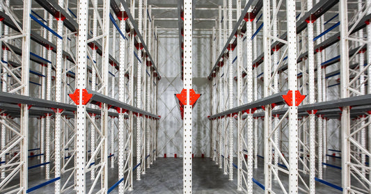 An aluminum cantilever rack system with red components is in an empty warehouse. Panel lights are on the ceiling.