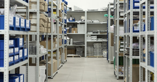 Blue plastic trays with white labels on them and cardboard boxes stacked neatly on industrial metal racks.