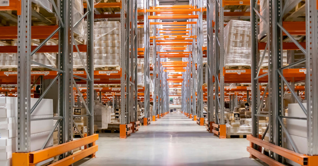 A large warehouse filled with industrial pallet racks that hold numerous stacks of boxed and plastic-wrapped goods.