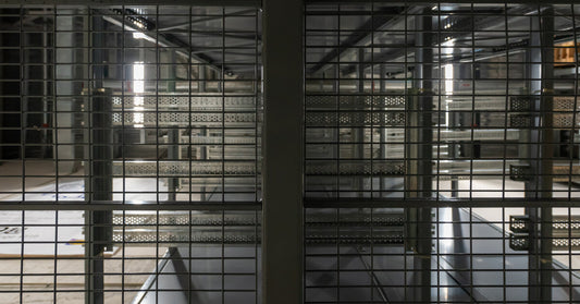A dimly lit warehouse is seen through one row of a wire mesh storage racking system with nothing on it.