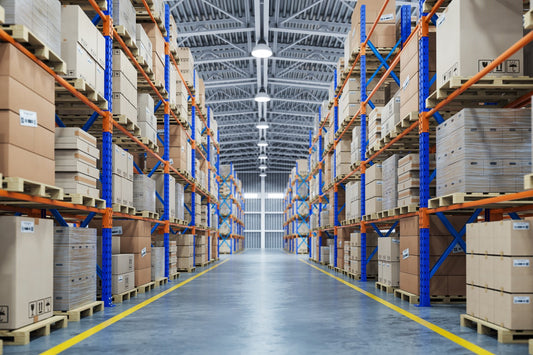 A warehouse worker wearing a hard hat and safety vest examining a row of racking, noting its condition on a clipboard.