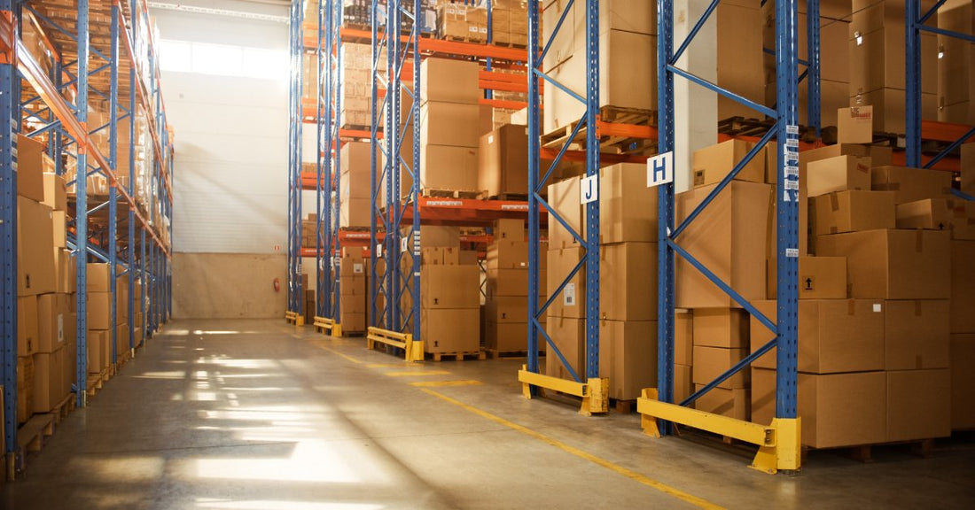 A warehouse containing pallet racks that hold multiple organized stacks of cardboard boxes. The rows are alphabetized.