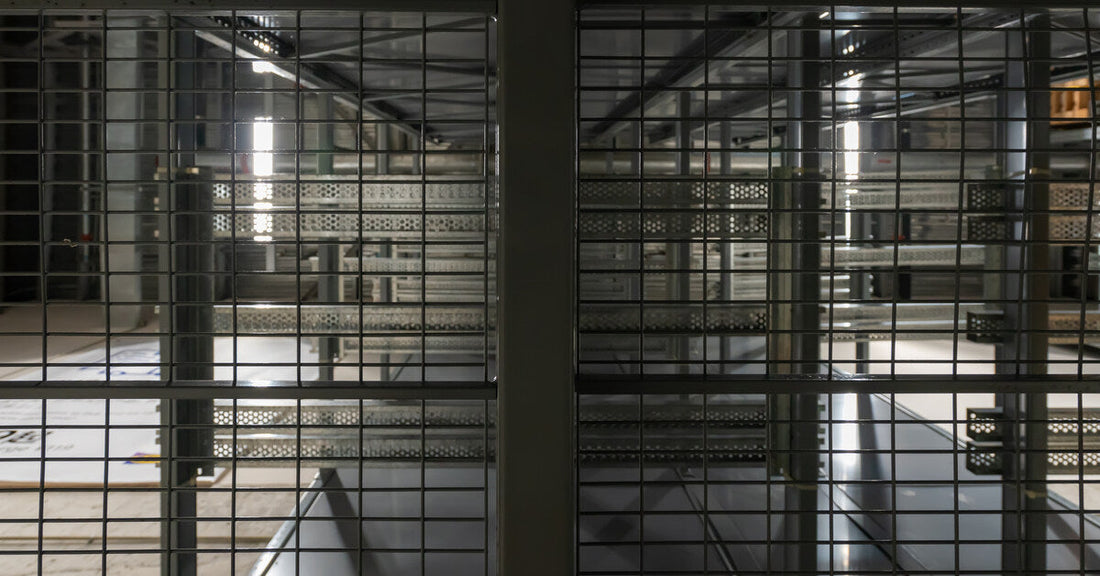 A dimly lit warehouse is seen through one row of a wire mesh storage racking system with nothing on it.