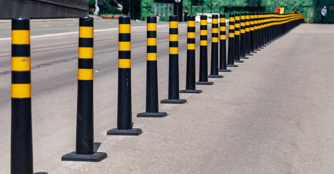 A line of black bollards with yellow lines on them. They are separating the road from the sidewalk.