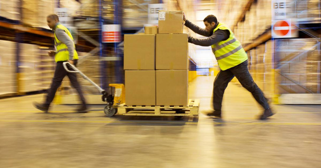Workers are moving a cart quickly to get a set of boxes across the warehouse.