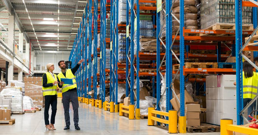 Two managers walking through a warehouse, inspecting the building. In front of them are large pallet racks.