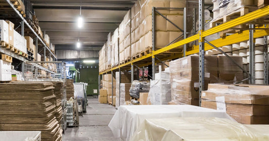 A warehouse with two sets of shelves on either side. There are packages stacked on the shelves and covered in plastic.