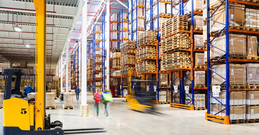 A large storage warehouse with tons of storage racks, each having a guard rail. There are workers and forklifts moving around the area.