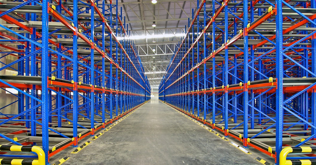 In a warehouse, two empty pallet racking systems stand in rows. The frames of the racking systems are blue and orange.