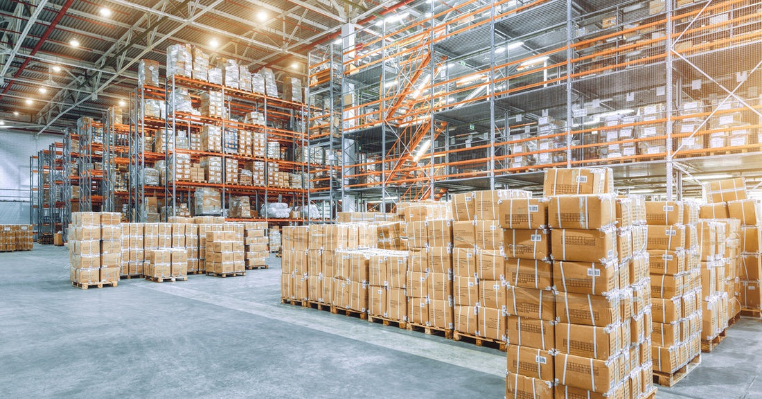 An industrial warehouse with packages stacked on pallet racks. Behind them are tall racks that are also holding cardboard boxes.