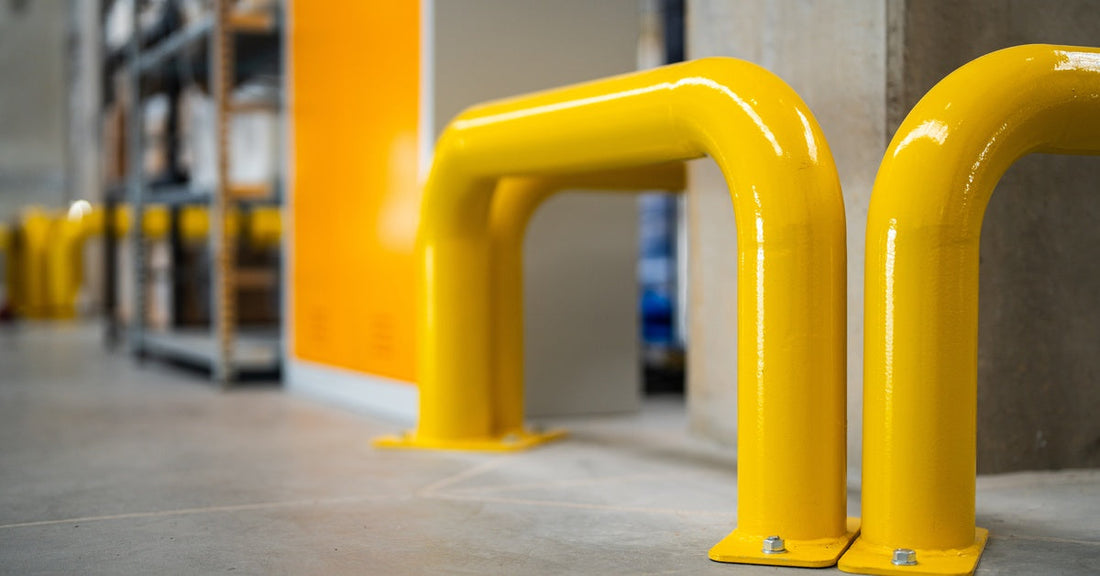 A thick yellow protective barrier screwed into the floor in an industrial setting. There is a shelf next to the barrier.