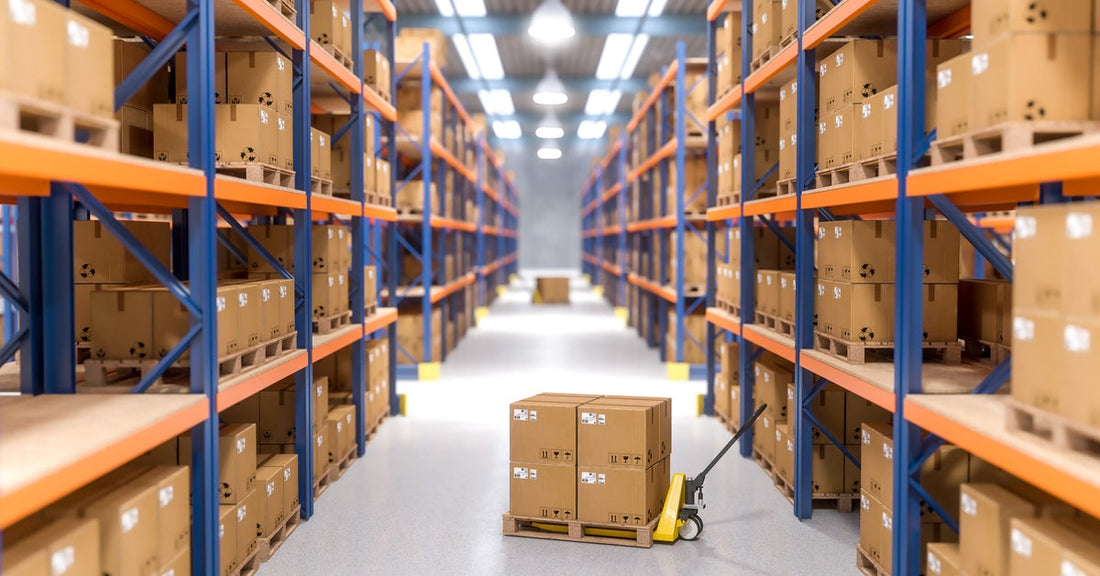 A row of shelves in a warehouse, filled with packages. In the center of the aisle is a dolly with packages on it.