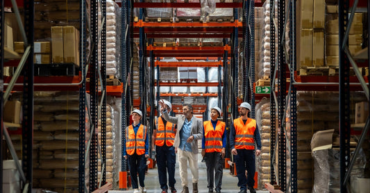 A warehouse manager leading his team through a facility with industrial racking. The workers are wearing safety gear.