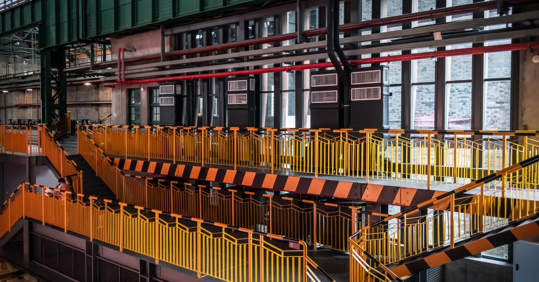 An industrial building with yellow guardrails. There are two sets of stairs going down to a lower level.
