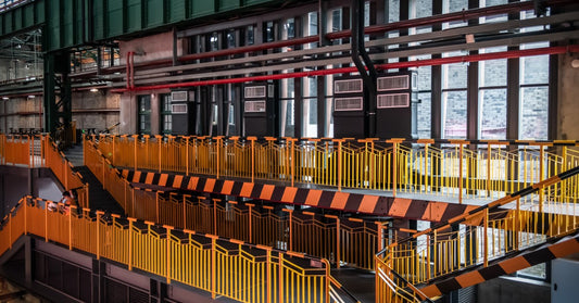 An industrial building with yellow guardrails. There are two sets of stairs going down to a lower level.