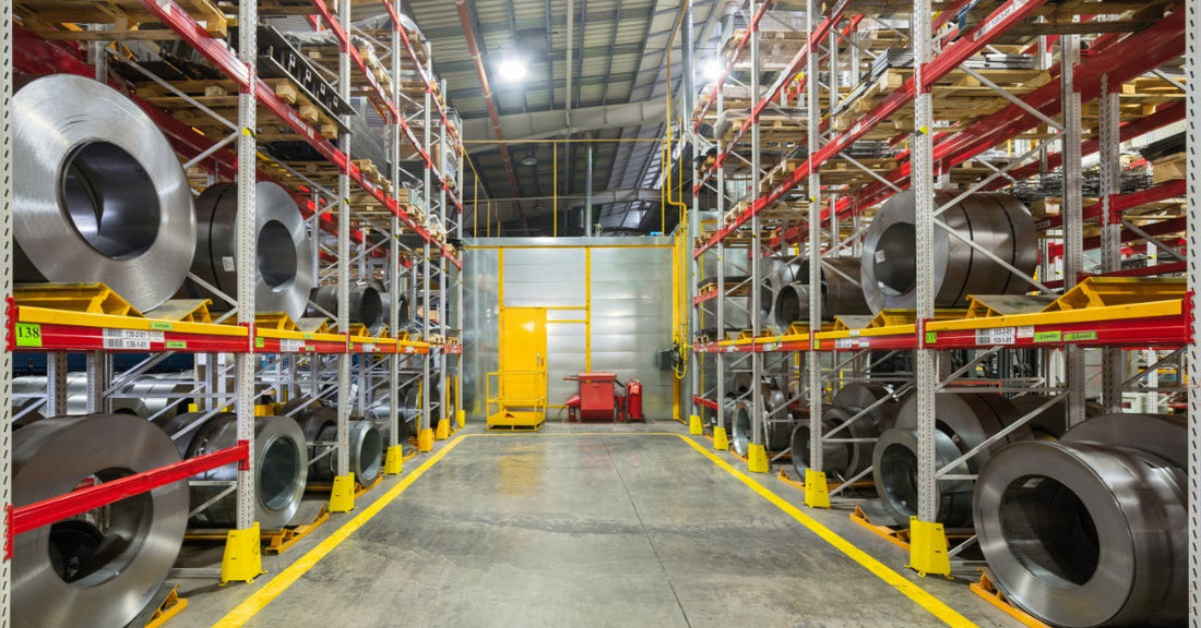 A row or tiered racking shelves storing large rolls or meta sheets. The warehouse holds raw materials.