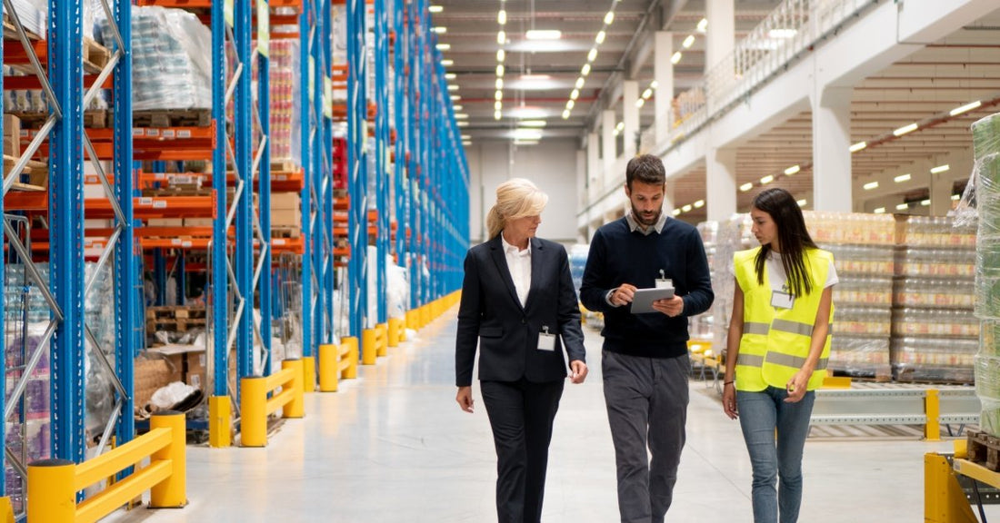 Managers walking through a warehouse with industrial shelving. They are with an employee and checking a tablet.