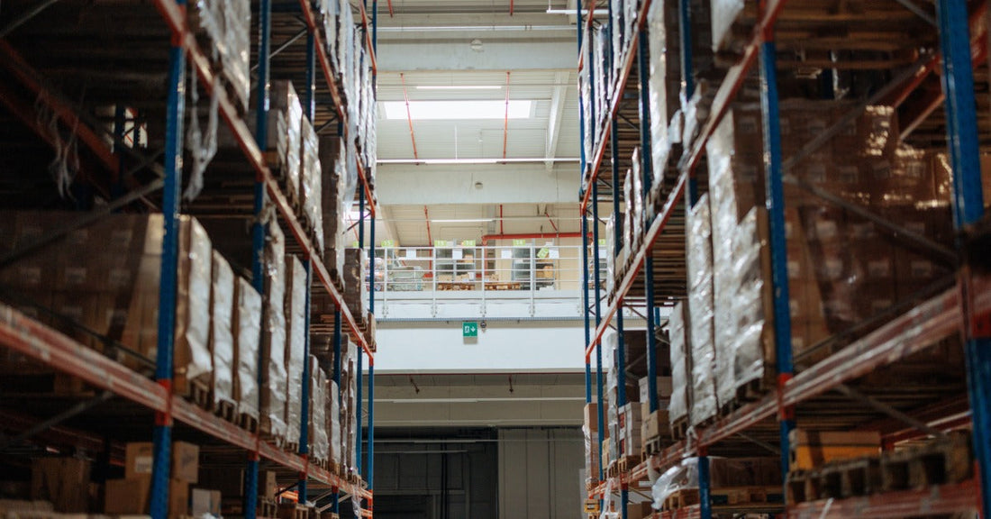 A large warehouse with industrial shelves holding inventory. There is a mezzanine level above the shelves.