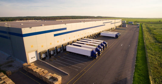 An aerial view of a distribution warehouse with several trucks parked at loading docks beside paved lanes.