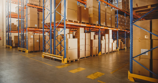 A large retail warehouse full of racks and shelves with goods packaged in brown cardboard boxes stacked together.