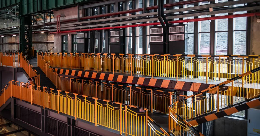 The interior of an industrial plant, with two stories of walkways and stairs featuring bright yellow safety railing.