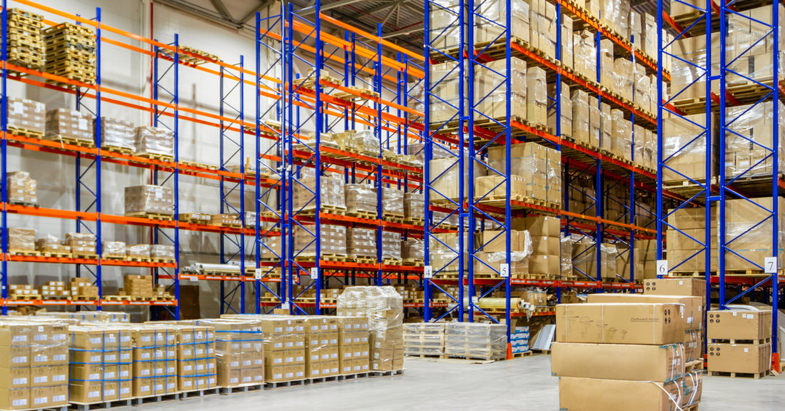 A warehouse with rows of blue and orange pallet racks. A few pallets of boxes are on the ground, waiting to be loaded.