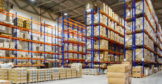 A warehouse with rows of pallet racks. The front racks are full while the back ones have space, and pallets are on the floor.