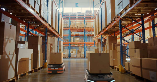 An aisle between racking systems in a warehouse. Two AGV robots carrying boxes travel through the aisle.