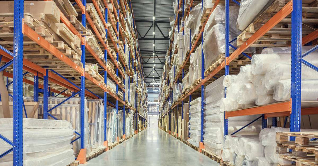 Two pallet racks and the clear aisle between them. The racks are mostly full and house various types of goods on wooden pallets.